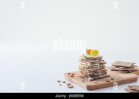 Rye crispy bread (Swedish crackers) stacked in the form of cake in layers with soft cheese, cherry tomatoes and rosemary, on wooden board, white backg Stock Photo