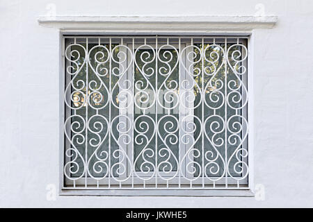 Window on the white wall. Figured frame of the window hole. Iron wrought-iron lattice curly painted white Stock Photo