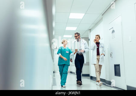 Group of medics with clipboard discussing along hospital corridor. Doctor and nurse briefing medical report with female colleague talking on mobile ph Stock Photo