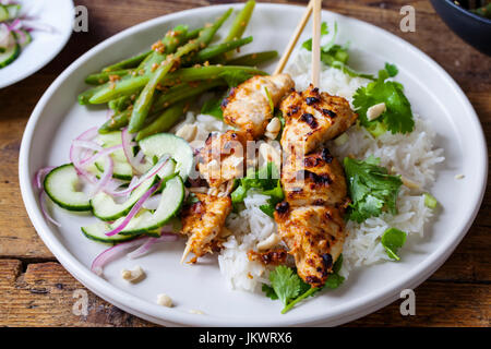 Satay chicken skewers with rice, cucumber salad and green beans Stock Photo