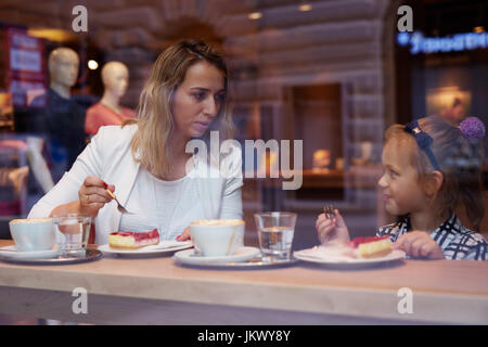 Young mother and daughter spending time in cafe and eating cake Stock Photo