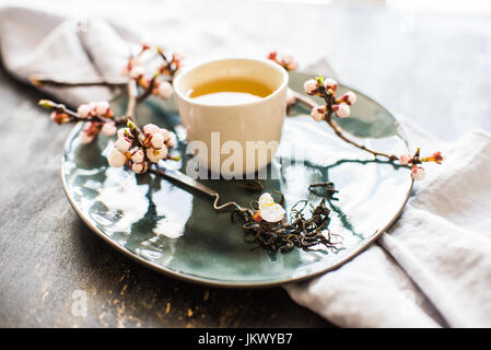 Cup of green tea and peach blossom on dark rustic table as a spring time concept Stock Photo