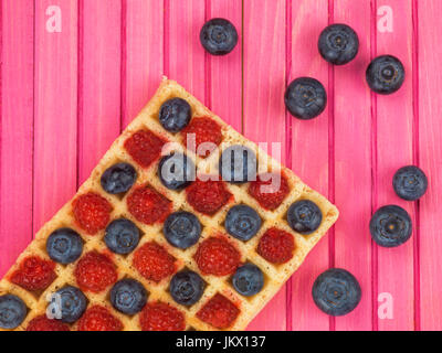 Raspberries and Blueberries on a Toasted Waffle Against a Pink Wooden Background Stock Photo