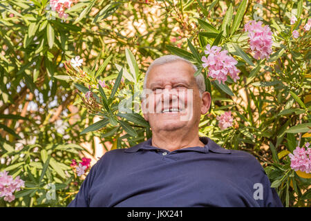 portrait of smiling elderly on a background of Oleander flowers and plants in home garden Stock Photo