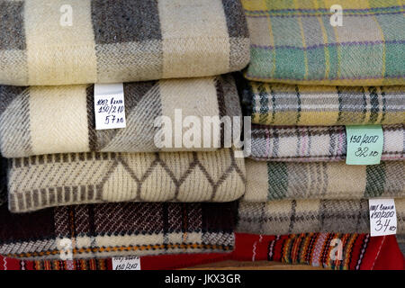 Stacked folded blankets for sale with price tags in bulgarian language. The foreign text translates as 100% wool Stock Photo