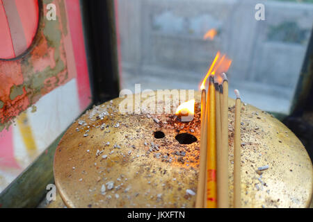 Close up of an incense burning up over a bronze tray with fire in the middle at Wong Tai Sin Temple, Hong Kong, China Stock Photo