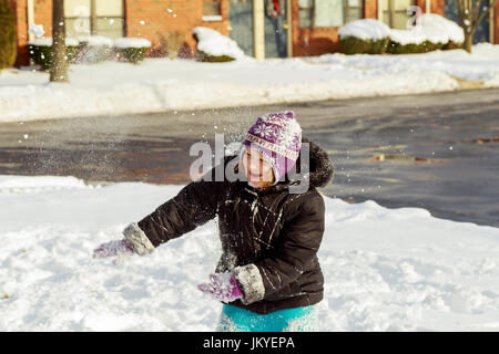 Little girl shoveling snow on home drive way. Beautiful snowy garden or front yard. Child with shovel playing outdoors in winter season. Family removi Stock Photo