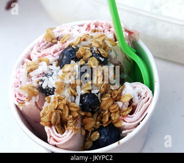 Stir fried ice rolls made with strawberry ice cream, topped with blueberries, granola and coconut in a bowl Stock Photo