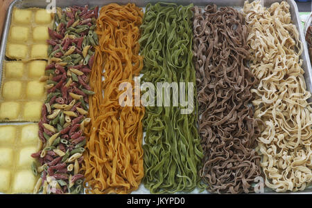 Fresh uncooked colorful ravioli, penne, and fettuccine pasta in a tray Stock Photo