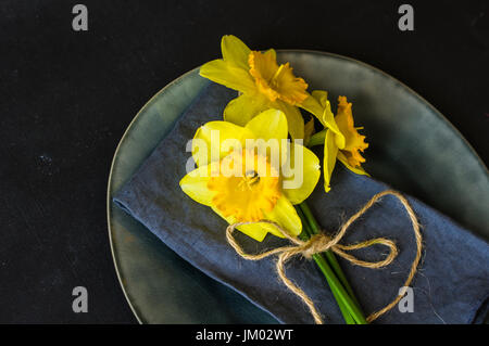 Spring table setting for Easter dinner with bright plates and bright yellow daffodils on a wooden table Stock Photo