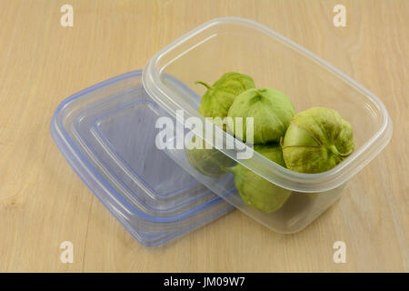 Green tomatillos in husks in plastic refrigerator storage container on wooden table Stock Photo