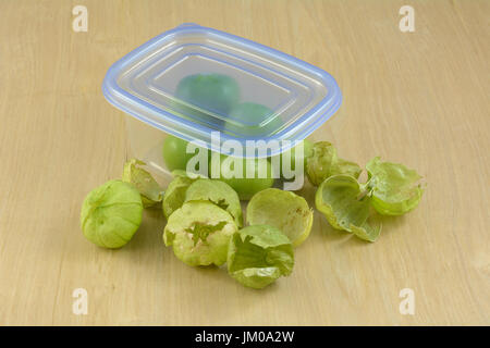 Green tomatillos in husks in plastic refrigerator storage container on wooden table Stock Photo