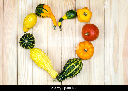 Many different pumpkins lie in heart shape on wood Stock Photo