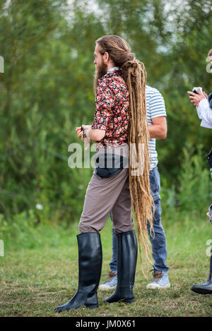 BONTIDA, ROMANIA - JULY 16, 2017: Young blonde man with long rasta dreadlocks and black horseriding boots enjoying Electric Castle festival Stock Photo