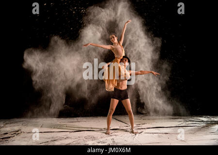 Attractive couple ballet dancer with white powder in the air against black background Stock Photo