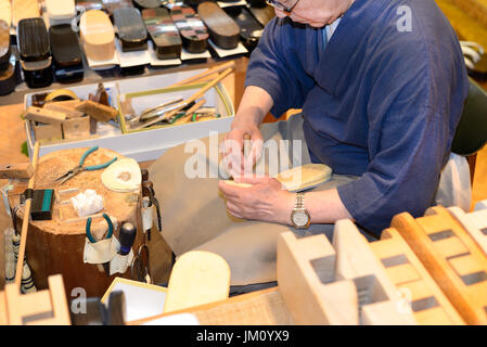 KYOTO, JAPAN - July 24, 2017: A craftsman attaches a strap to a zori--traditional Japanese sandals to be worn with a kimono--in his geta and zori shop Stock Photo