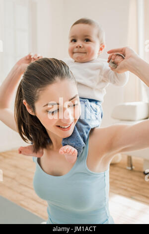 Portrait of young mother carrying her son piggyback at home Stock Photo