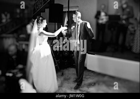 Newly married couple dancing on their wedding party with heavy smoke and multicolored lights on the background. Black and white photo. Stock Photo