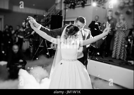 Newly married couple dancing on their wedding party with heavy smoke and multicolored lights on the background. Black and white photo. Stock Photo