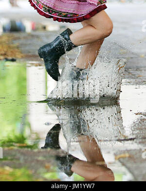 Berlin, Germany. 25th July, 2017. A young woman jumps over a rain puddle at Karl Marx Street in Berlin, Germany, 25 July 2017. According to meteorologists the following days will remain rainy with temperatures around 17 degrees. Photo: Wolfgang Kumm/dpa/Alamy Live News Stock Photo