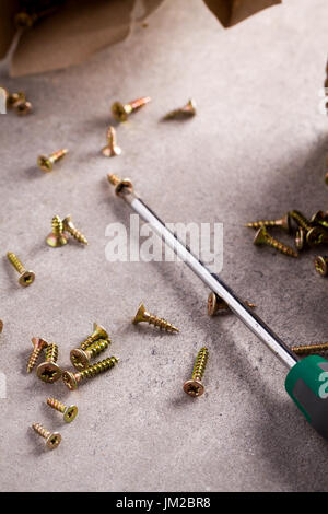 Scattered small screws and lying down screwdriver on floor. Stock Photo