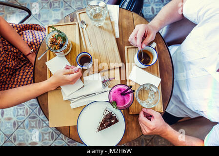 Couple of Man and woman on date having breakfast in the morning in cafe. Granola, chocolate cake, smoothie and hot coffee on the table. Flatlay, selective focus. Stock Photo