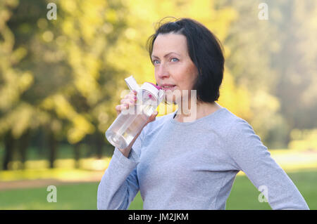 Sporty mature woman drinking water outdoor on sunny day in the park. Healthy lifestyle Stock Photo