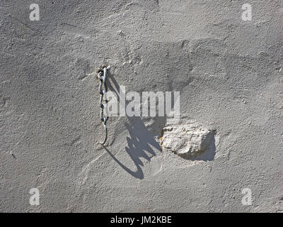 white painted metal chain hanging on textured white rendered wall casting dramatic oblique shadow diagonally on uneven surface in Cumbria, England, UK Stock Photo