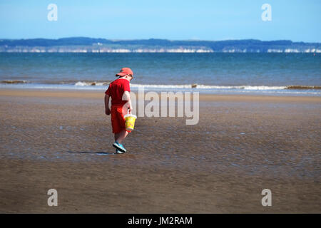 Young boy in red heading for the sea at low tide with a bucket. Stock Photo