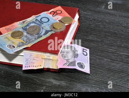 Australian dollars, Australian coins, book on table. Dollar five, ten dollar 20 notes. Coins 20 Cents, 50 Cents. Dollar 1 coin and Dollar 2 coin Stock Photo