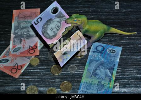 Selective focus on Australian dollar five note in dinosaur's mouth with out of focus Australian coins and ten dollar note, twenty dollar on the table Stock Photo