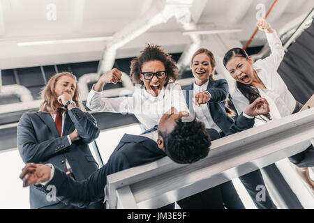 Three young angry businesswomen punishing businessman lying on table, business team meeting concept Stock Photo