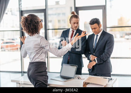 Young businesswoman gesturing and arguing with coworkers in office, business team meeting concept Stock Photo