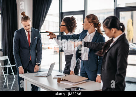 Three angry young businesswomen pointing with fingers at upset businessman in office, business team meeting concept Stock Photo
