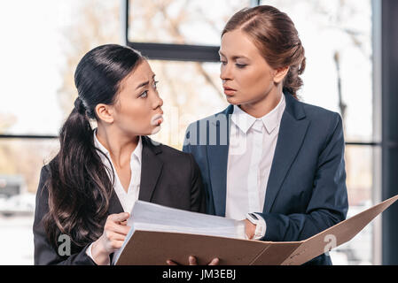 Two young businesswomen working together with folder and looking at each other, business team working concept Two young businesswomen working together with folder and looking at each other, business team working concept