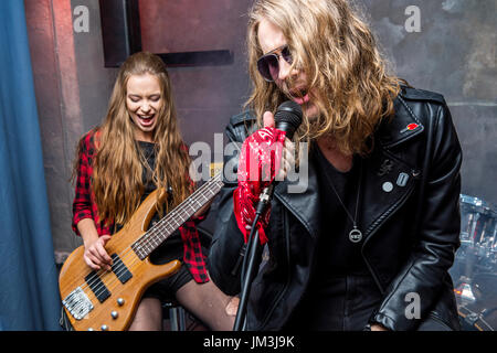 man singing in microphone with woman playing guitar, hard rock music concept Stock Photo