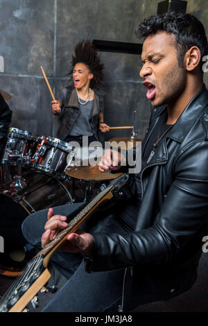 side view of man playing guitar with woman playing drums, hard rock music concept Stock Photo