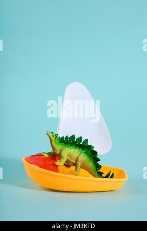 A dinosaur lost at sea on a toy boat like a noah's ark metaphor. Minimal Poetic still life photography Stock Photo