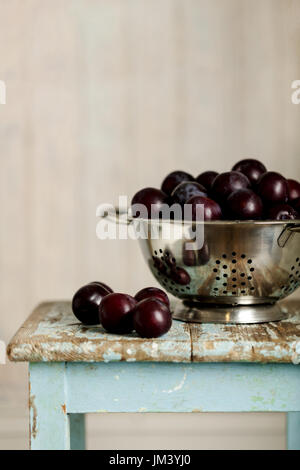 Ripe plums in a colander on a wooden background. Selective focus. Stock Photo