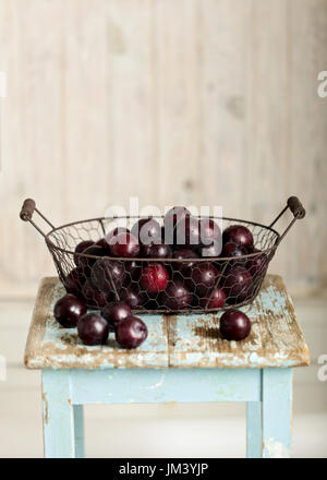 Ripe plums in a basket on a wooden background. Selective focus. Stock Photo