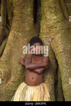 Little girl with a grass skirt standing in front of banyan tree roots, Tanna island, Yakel, Vanuatu Stock Photo