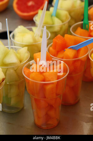 Street food, selection of fruit salads, slices of cut fresh ripe yellow and orange cantaloupe melon cubes in plastic cups with forks at retail market  Stock Photo