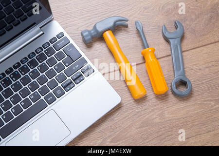 Concept of repair and maintenance on a laptop computer with a small hammer, screwdriver and spanner alongside the open notebook on a desk Stock Photo