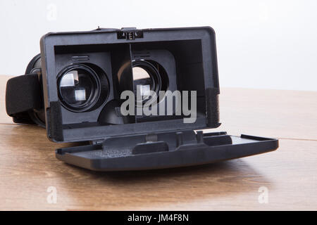 Open 3d VR virtual reality goggles or headset showing the optical lenses for creating simulated three-dimensional environments on a wooden desk in a c Stock Photo