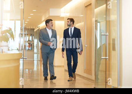 Two businessmen, one young and one mature, talking seriously while walking together in a modern office building foyer Stock Photo