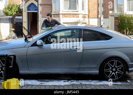 young man cleaning his car with pressure washer and sponge england uk Stock Photo