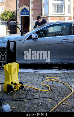 young man cleaning his car with pressure washer and sponge england uk Stock Photo