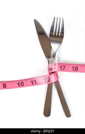 Crossed cutlery fork and knife bandaged with red measuring tape marked in inches, symbolising loosing weight fitness diet concept, isolated on white b Stock Photo