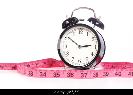 Classic black alarm clock showing ten minutes to three and pink measuring tape marked in inches, close-up front view isolated on white background with Stock Photo