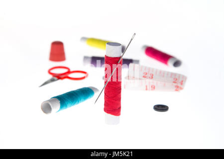 focus on red thread and needle with other sewing kit items in background Stock Photo